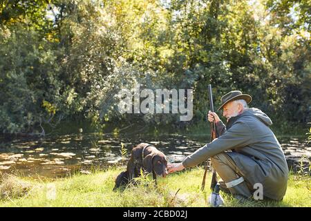 Ruhen Sie sich vor der Jagd aus. Jäger Mann auf See, hält Gewehr Stockfoto