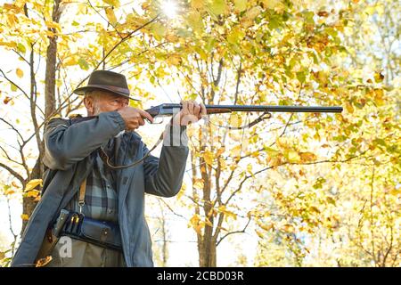 Konzentrierter Jäger hält Gewehr und wartet auf Beute, Jäger schießen im Herbstwald. Jagdsaison Stockfoto