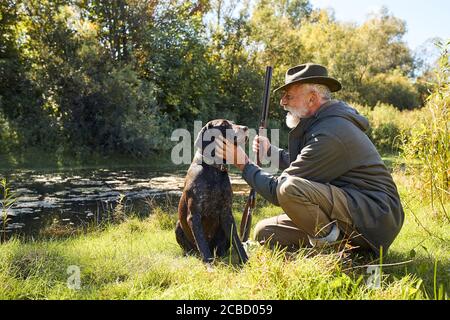 Ruhe nach der Jagd. Gute Arbeit, erfolgreiche Jagd auf See. Bärtiger Mann nach der Jagd auf Enten streicheln seinen Hund Stockfoto