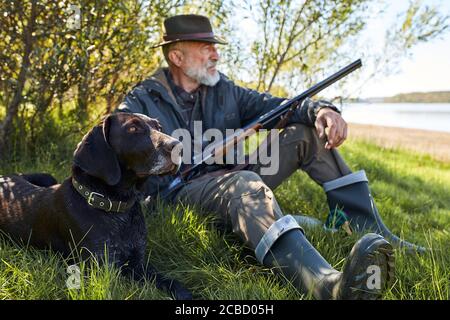 Auf der Suche nach Trophäe mit Hund. Älterer Mann bereit zur Jagd. Sitzen und ruhen vor der Jagd Stockfoto