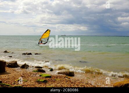 Windsurfer mit bunten Segeln auf der Solent vor der Küste von Strandgurnard Isle of Wight in einer steifen Brise unter Ein stimmungsvoller Himmel Stockfoto