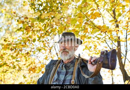 Zufriedene Jäger tragen Gewehr auf der Schulter, Blick auf Kamera.Herbst Natur Hintergrund. Jagd maskulin, Hobby und Freizeitkonzept Stockfoto