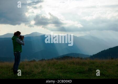 Mädchen Fotografin in den Bergen schießt die Landschaft auf der Hintergrund der Sonnenstrahlen an einem bewölkten Tag Stockfoto