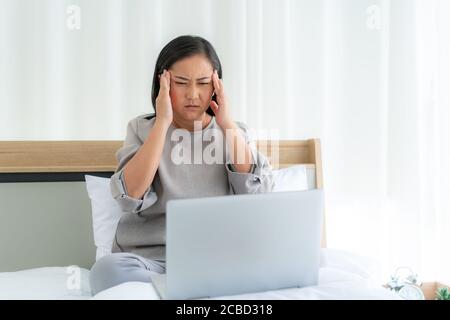 Asiatische Frau im weißen Bett sprechen mit Arzt mit Tele Gesundheitstechnologie, während sie auf einem Sofa sitzen und Kopfschmerzen im Schlafzimmer zu Hause, während sie duri krank Stockfoto