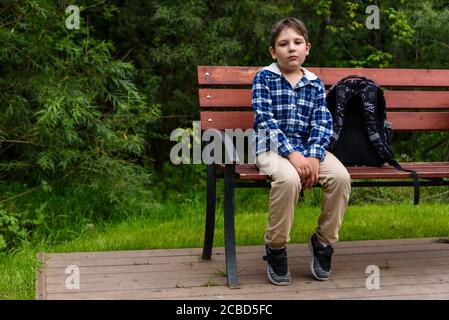 Trauriger Schuljunge mit Rucksack auf einer Straßenbank sitzend Und denken Stockfoto