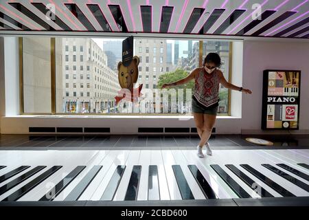 New York City, USA. August 2020. Liza Slack, zu Besuch aus Florida, spielt auf dem großen Toe Tap Floor Piano, berühmt gemacht in dem Film "Big" im neu eröffneten berühmten Spielwarenladen FAO Schwarz im Rockefeller Center in New York, NY, 12. August 2020. Die FAO hat obligatorische Masken für alle, die das Geschäft betreten, einschließlich Kinder, soziale Distanzmarkierungen eingeführt und hat Mitarbeiter, wenn möglich, Oberflächen kontinuierlich reinigen und desinfizieren lassen. (Anthony Behar/Sipa USA) Quelle: SIPA USA/Alamy Live News Stockfoto