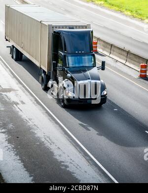 Stylish Heavy Loaded klassisch schwarz big Rig semi-Truck mit Dachspoiler, der kommerzielle Ladung am Container auf Sattelauflieger transportiert Laufen auf der stra Stockfoto