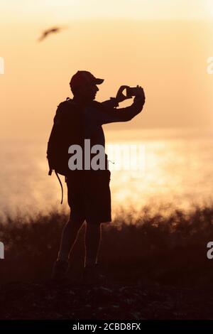 Männlicher Tourist, der fotografiert, bei Sonnenuntergang silhouettiert, Ozean im Hintergrund, Darwin Bay, Isla Genovesa, Galapagos, Ecuador 27. November 2017 Stockfoto