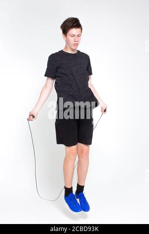 Ein junger Mann in einem schwarzen Sport-T-Shirt und Shorts, blaue Turnschuhe, üben Springseil isoliert auf weiß. Stockfoto