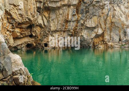 Ein grüner See und eine felsige Klippe mit Löchern in verlassenen Stollen. Tuim ist ein Sinkhole an der Stelle einer verlassenen Kupfer- und Wolframerzmine. Stockfoto