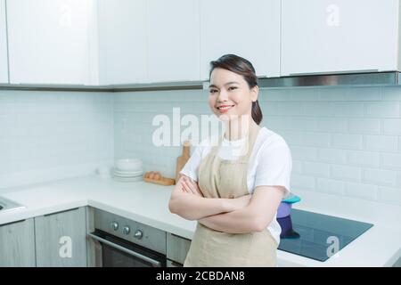 Porträt einer jungen Frau, die mit gekreuzten Armen vor Küchenhintergrund steht