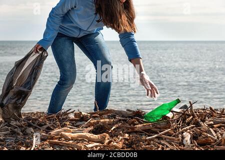 Frau reinigt Müll am Strand, holt die Flasche. Ökologie, Tag der Erde, Reinigung des Territoriums Konzept. Stockfoto