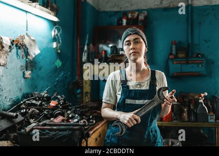 Das Konzept von Kleinunternehmen, Feminismus und Frauengleichheit. Eine junge Frau in Overalls posiert mit einem großen Schraubenschlüssel in den Händen. Stockfoto