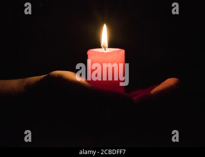 Weibliche Hände halten eine brennende Kerze im Dunkeln Stockfoto