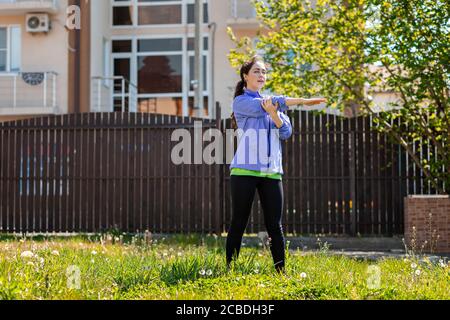 Eine junge Frau in Sportkleidung macht Yoga in ihrem Hof, auf dem Gras. Im Freien. Das Konzept eines gesunden Lebensstils und Heimsports. Stockfoto