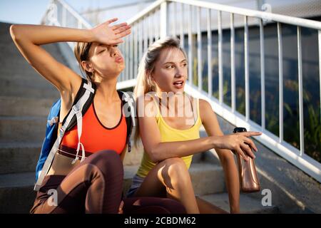 Schöne Frauen in Sportbekleidung Trinkwasser, sprechen und ruhen nach dem Training im Freien Stockfoto