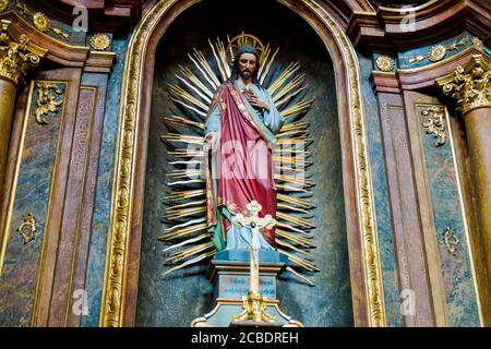 Eine niedrige Ansicht einer bemalten hölzernen Jesus Skulptur mit Lichtstrahlen in einer Nische einer Kirche. In Wien, Österreich. Stockfoto