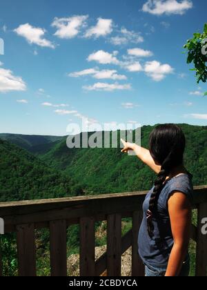 Eine afro-asiatische Frau von hinten zeigt auf die Berglandschaft. Während der Ferien, Touristen gerne eine Pause zu nehmen, um die Natur zu bewundern Stockfoto