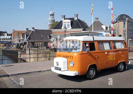 Orange Retro Volkswagen Transporter mit weißem Dach und eingerichtet als Camper mit weißen Vorhängen fährt über den Blokjesbrug in Lemmer, Friesland Stockfoto