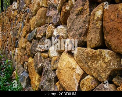 Trockene Steinwand, Nahaufnahme. Steinmauer in der Nähe des Hauses in der Landschaft bei Sonnenuntergang. Eine traditionelle Trockensteinmauer auf dem Feld. Steinwandmuster. Stockfoto