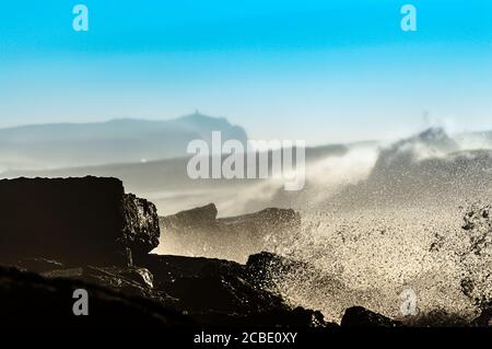 Nahaufnahme von Felsen und Wellen, die am Ufer brechen Auf einem blauen Himmel Hintergrund Stockfoto