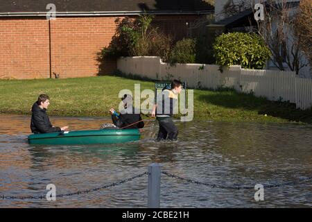 Boys peddeln ein Boot durch überflutete Slough Road im Dorf Datchet, Berkshire, nachdem die Themse an ihren Ufern platzte. Datchet, Berkshire, Großbritannien. Februar 2014, 10 Stockfoto