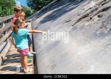 Kinder, die auf Felsen geschnitzte Rupestrian-Zeichnungen betrachten, Naquane Park, Capo di Ponte, Valcamonica, Lombardei, Italien Stockfoto