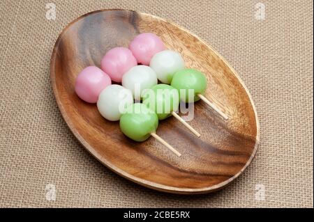Japanische traditionelle süße Dango Mochi auf Holzplatte mit grünem Tee. Isoliert auf Jute-Hintergrund. Nahaufnahme. Draufsicht. Stockfoto