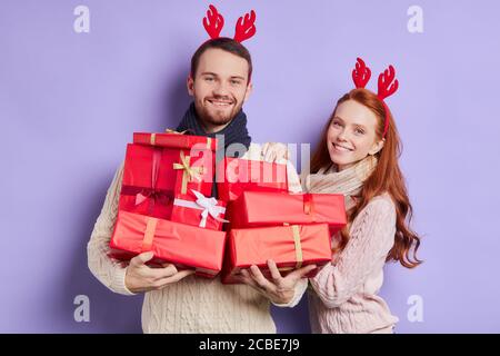 Angenehme schöne Frau mit Füchshaar und charmantes Lächeln zusammen mit schönen Freund stehen, hält Weihnachtsgeschenke in den Händen, Vorbereitung Geschenk Stockfoto