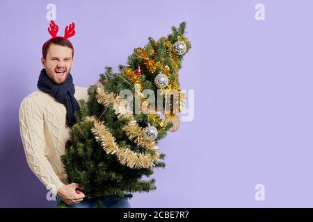 Schöner hübscher Mann mit dickem Bart, trägt einen warmweißen Pullover, hat einen stylischen Strickschal am Hals, mit rotem Horn am Kopf und schaut mit der Kamera an Stockfoto