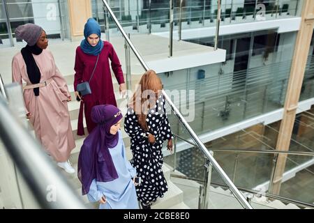 Junge muslimische, fröhliche Geschäftsreisende, Frauen in nationalen arabischen Kleidern, besuchen das Business Center und plaudern die Treppe hinunter über ihr Fu Stockfoto