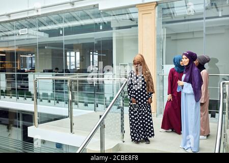 Multikulturelle Gruppe arabischer Studentinnen, die in nationalen Kleidern und Schals die Treppe der Universität erklimmen und Ideen mit jedem anderen teilen Stockfoto