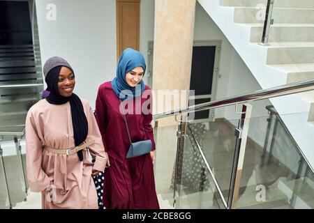 Junge muslimische, fröhliche Geschäftsreisende Frauen in nationalen arabischen Kleidern besuchen das Business Center und unterhalten sich über ihren Futur Stockfoto