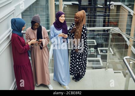 Gruppe von multirassischen muslimischen Geschäftsfrau chatten, Newsfeed auf dem Smartphone zu überprüfen, während Pause, stehend im Business Center Stockfoto