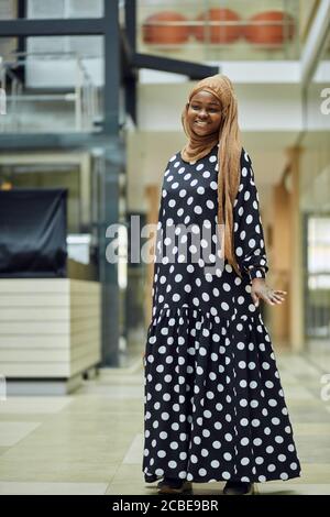 Lächelnde junge islamische afrikanische Frau trägt modisches Kopftuch und Kleid Auf einer U-Bahn-Station mit einer Tasche in Ihre Hand Stockfoto