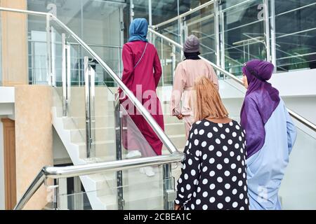 Eine multikulturelle Gruppe arabischer Studentinnen, die in nationalen Kleidern und Schals die Treppe der Universität erklimmen und Ideen mit jedem anderen teilen Stockfoto