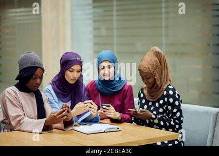 Asiatische islamische Frauen in hellen Hijabs teilen Informationen vom Smartphone Während ihres Besuchs ein Seminar im Bildungszentrum Stockfoto