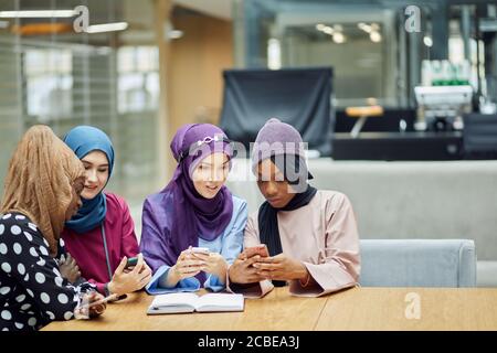 Arabian jung modisch in muslimischer Kleidung gekleidet Frauen beobachten auf Handy musikalischen Videoclip stehend zusammen im Einkaufszentrum - Millennials, ge Stockfoto