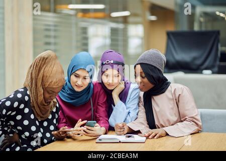 Islamische Reisebloggerin, die Informationen vom Smartphone mit ihr teilt Anhänger, während sie in der vierköpfigen Gruppe in der Hotellobby sitzen Stockfoto