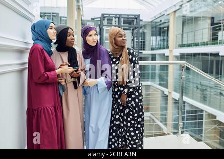 Gruppe von multirassischen muslimischen Geschäftsfrau chatten, Newsfeed auf dem Smartphone zu überprüfen, während Pause, stehend im Business Center Stockfoto