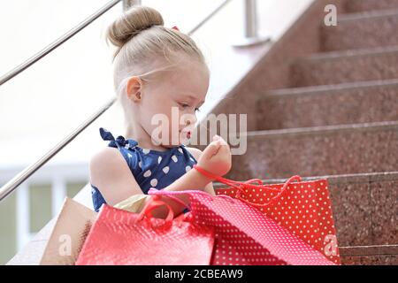 Kleines Mädchen sitzt mit farbigen Taschen auf den Stufen in der Mall. Stockfoto