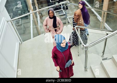 Multikulturelle Gruppe arabischer Studentinnen, die in nationalen Kleidern und Schals die Treppe der Universität erklimmen und Ideen mit jedem anderen teilen Stockfoto