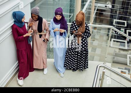 Gruppe von multirassischen muslimischen Geschäftsfrau chatten, Newsfeed auf dem Smartphone zu überprüfen, während Pause, stehend im Business Center Stockfoto