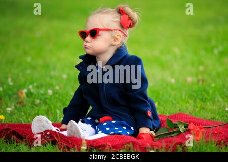 Kleines Mädchen sitzt auf dem Gras im Park tragen Sonnenbrille Stockfoto