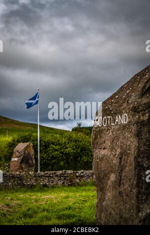 Steinmarkierungen an der Grenze zwischen Schottland und England mit Eine Saltyre Flagge und Sturmwolken im Hintergrund Stockfoto