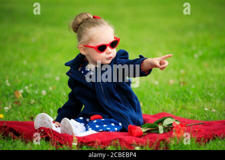 Kleines Mädchen sitzt auf dem Gras im Park tragen Sonnenbrille Stockfoto