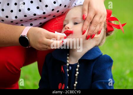 Mama wischt Gesicht von kleinen Mädchen Gesicht mit Lippenstift gefärbt Stockfoto