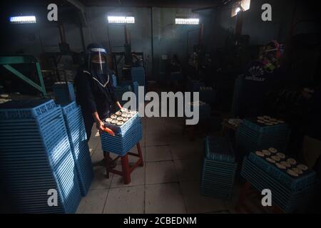 (200813) -- WEST JAVA, 13. August 2020 (Xinhua) -- EIN Arbeiter, der einen Gesichtsschutz trägt, hält in einer Cracker-Fabrik in Depok, West Java, Indonesien, ein Tablett mit ungekochten Crackern. 13. August 2020. Indonesien wird 9 Millionen kleine und mittlere Unternehmen (KMU) mit Working Capital unterstützen, um ihnen zu helfen, Unternehmen wiederzubeleben, die von der neuartigen Coronavirus-Pandemie zerstört wurden, sagte ein Minister hier am Mittwoch. ( Xinhua/Agung Kuncahya B.) Stockfoto