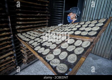 (200813) -- WEST JAVA, 13. August 2020 (Xinhua) -- EIN Arbeiter, der eine Gesichtsmaske trägt, hält gedämpfte Cracker, die in einem Ofen in einer Cracker-Fabrik in Depok, West Java, Indonesien, getrocknet werden, 13. August 2020. Indonesien wird 9 Millionen kleine und mittlere Unternehmen (KMU) mit Working Capital unterstützen, um ihnen zu helfen, Unternehmen wiederzubeleben, die von der neuartigen Coronavirus-Pandemie zerstört wurden, sagte ein Minister hier am Mittwoch. ( Xinhua/Agung Kuncahya B.) Stockfoto