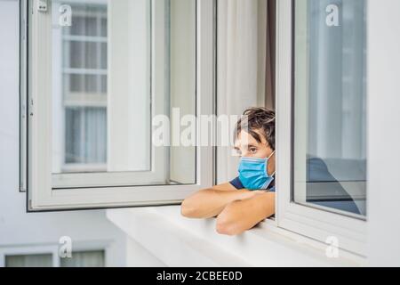 Extrem müde junger Mann, der aus dem Fenster schaut, allein zu Hause. Selbstisolation zu Hause, Quarantäne wegen Pandemie COVID 19. Psychische Probleme in Stockfoto